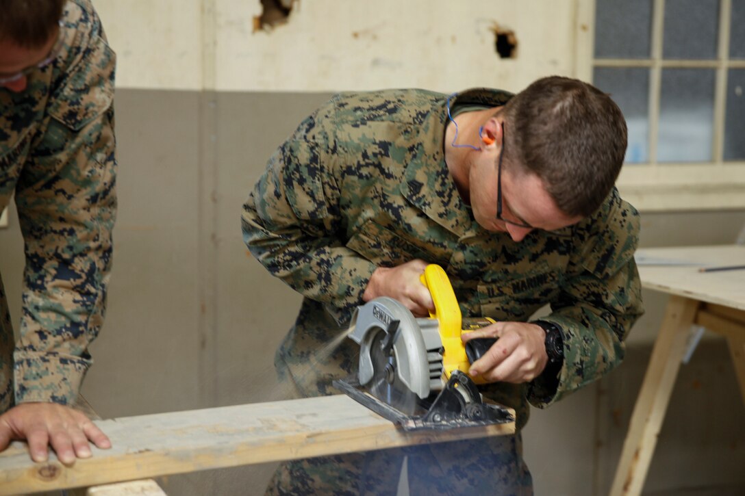 U.S. Marine Sgt. Derek R. Rush (right), squad leader with Headquarters and Service Company, 6th Engineer Support Battalion, 4th Marine Logistics Group, uses a circular saw to practice cutting a wooden plank at a construction site during exercise Red Dagger at Fort Indiantown Gap, Pa., May 19, 2018.