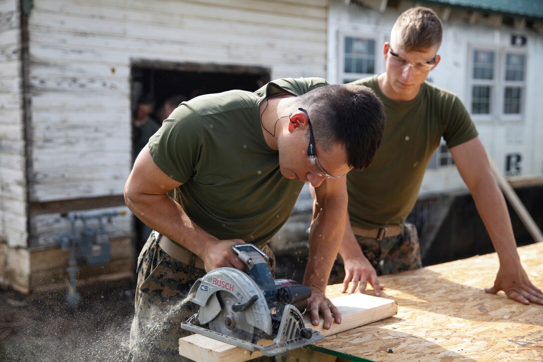 U.S. Marine Lance Cpl. Dylan A. Hudson (left), combat engineer with Engineer Company C, 6th Engineer Support Battalion, 4th Marine Logistics Group, cuts a wooden plank with a circular saw while U.S. Marine Private First Class Jeffrey Beasley (right), combat engineer with ECC, 6th ESB, 4th MLG, holds the table for stability at a construction site during exercise Red Dagger at Fort Indiantown Gap, Pa., May 20, 2018.