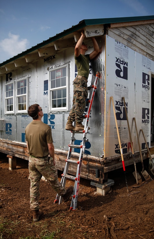 U.S. Marine Private First Class Jeffrey Beasley (top), combat engineer with Engineer Company C, 6th Engineer Support Battalion, 4th Marine Logistics Group, makes markings on a roof frame as British Army Spr. William Staniforth, commando with 131 Commando Squadron Royal Engineers, British Army, holds the ladder in place at a construction site during exercise Red Dagger at Fort Indiantown Gap, Pa., May 20, 2018.