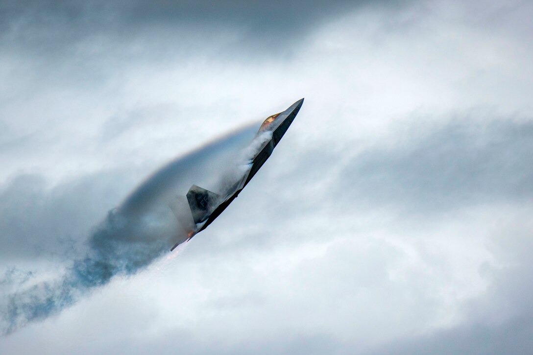 A jet flies in an upward curve, creating curved plues of smoke around its body.
