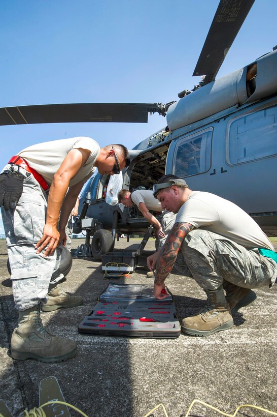 Airmen inspect tools before replacing a tire on a helicopter.