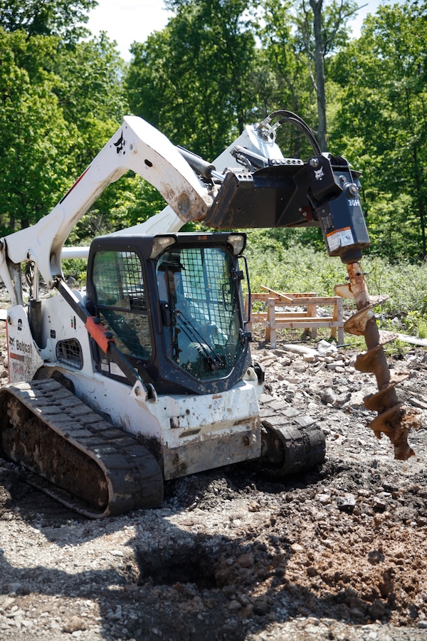U.S. Marine Lance Cpl. Mitchell R. Neimann (left), heavy equipment operator with Engineer Company C, 6th Engineer Support Battalion, 4th Marine Logistics Group, operates an Bobcat auger to dig a hole at a construction site during exercise Red Dagger at Fort Indiantown Gap, Pa., May 21, 2018. Exercise Red Dagger is a bilateral training exercise that gives Marines an opportunity to exchange tactics, techniques and procedures as well as build working relationships with their British counterparts. (U.S. Marine Corps photo by Sgt. Melanie Wolf/Released)