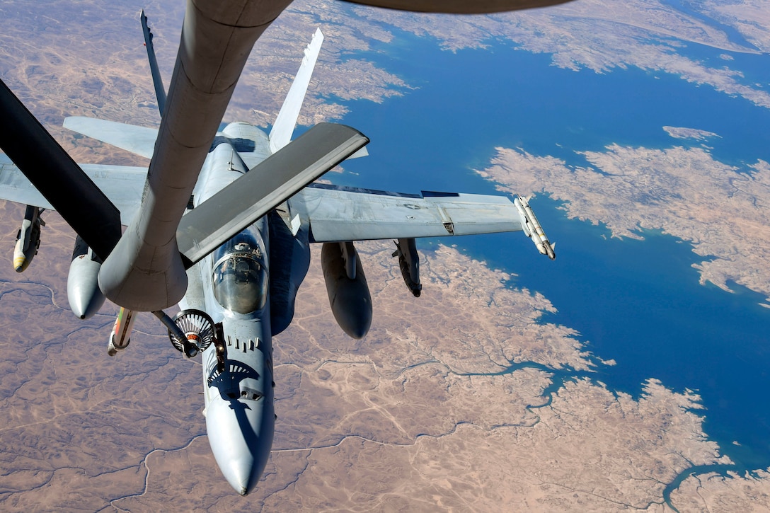 An aircraft receives fuel while flying over a river.