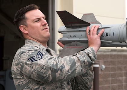 Staff Sgt. Randall Stoiner, a 90th Aircraft Maintenance Unit load crew chief, lifts a weapon used in the Wing Weapons Load Crew 1st Quarter Competition May 18, 2018, at Joint Base Elmendorf-Richardson, Alaska. The quarterly competition consists of two AMU weapons-section teams going head-to-head for time and accuracy. A weapons load crew is a group of three people responsible for preparing and loading munitions onto an aircraft.