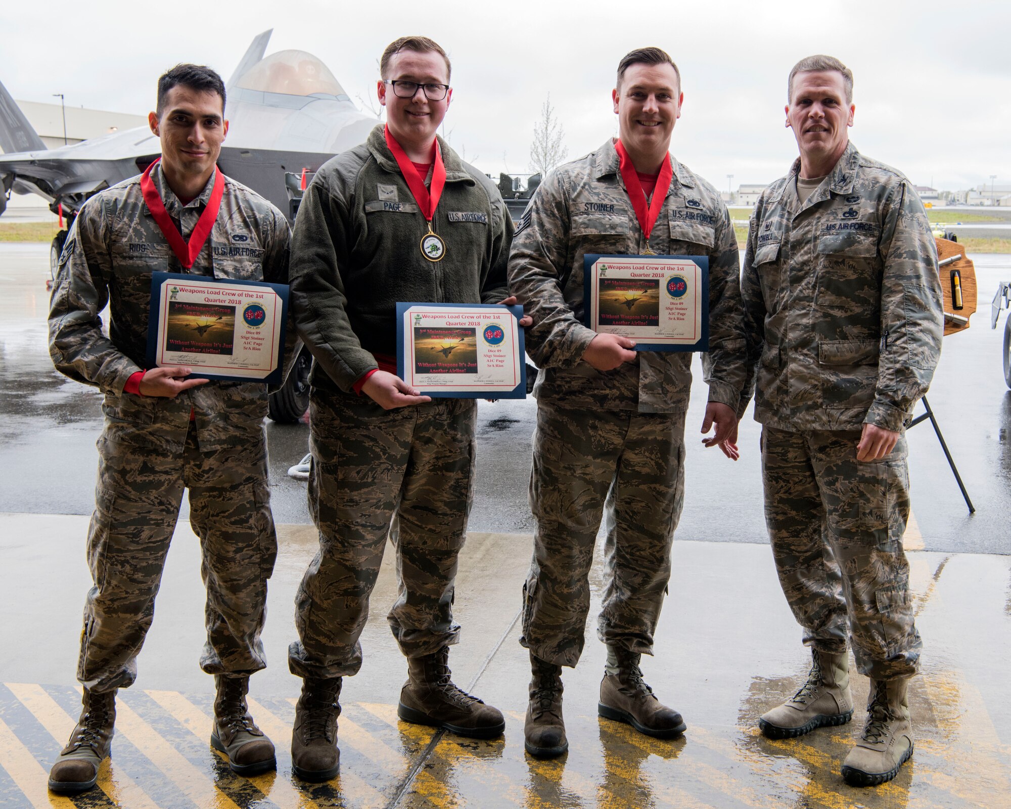 U.S. Air Force Col. Mathew Powell, commander of the 3rd Maintenance Group, stands with Staff Sgt. Randall Stoiner, Airman 1st Class Joseph Page and Senior Airman Justin Rios as they are recognized as winners of the Wing Weapons Load Crew 1st Quarter Competition May 18, 2018, at Joint Base Elmendorf-Richardson, Alaska. A weapons load crew is a group of three people responsible for preparing and loading munitions onto an aircraft.