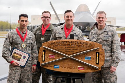 U.S. Air Force Col. Mathew Powell, commander of the 3rd Maintenance Group, presents a trophy to Staff Sgt. Randall Stoiner, Airman 1st Class Joseph Page and Senior Airman Justin Rios as they stand in front of an F-22A Raptor after the Quarterly Wing Weapons Load Crew Competition May 18, 2018, at Joint Base Elmendorf-Richardson, Alaska. Powell was congratulating the weapons load crew from the 90th Aircraft Maintenance Unit Weapons Section for winning the competition.