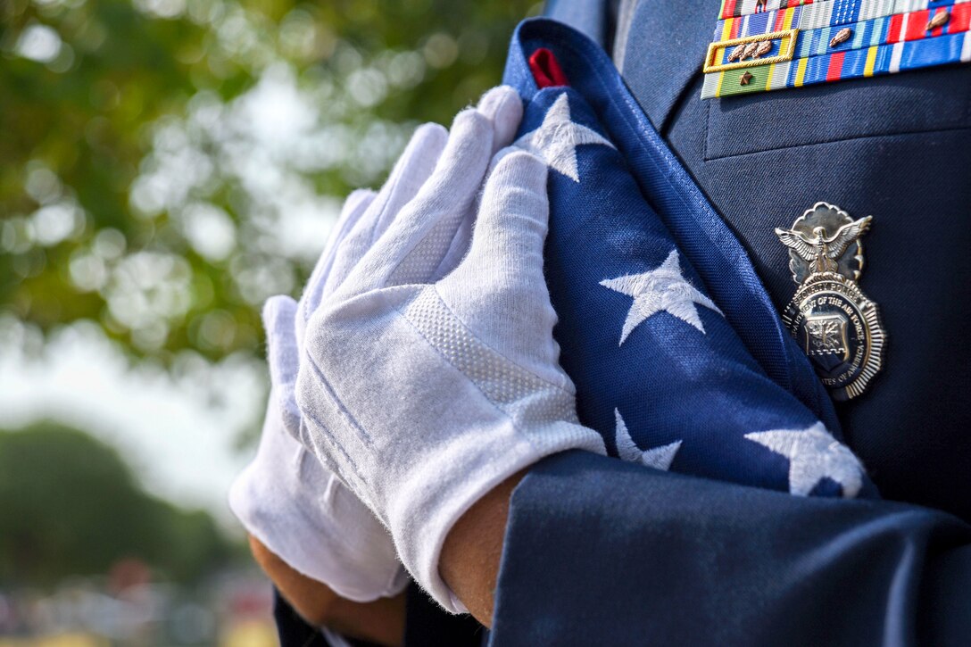 An airman's white-gloved hands hold a U.S. flag folded into a triangle against his chest.