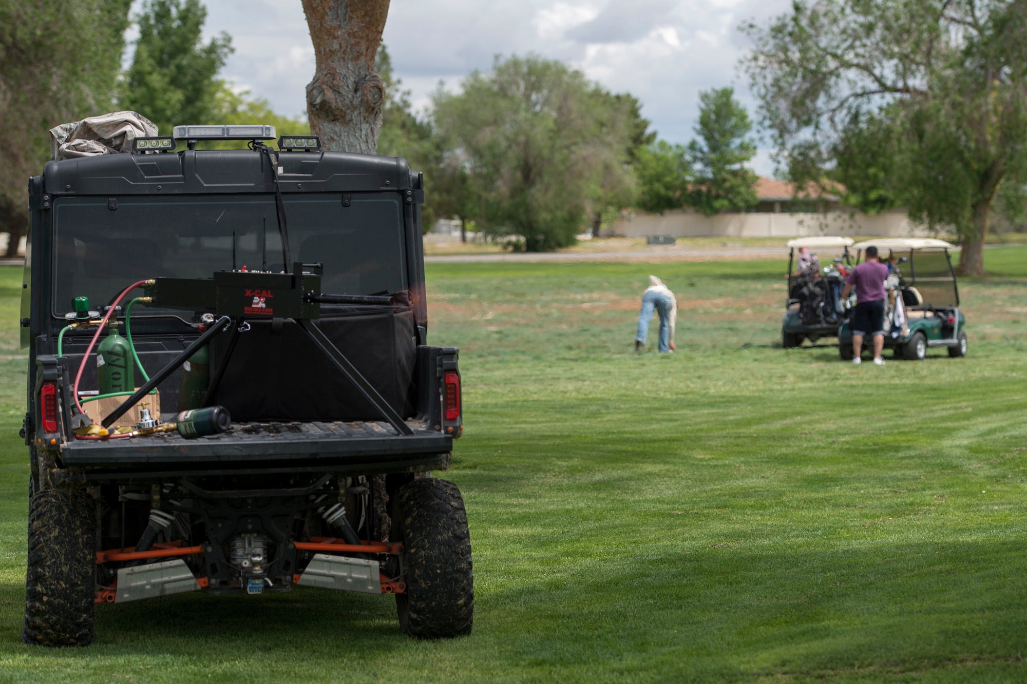 A photo of competitors playing golf while a simulated machine gun fires behind them May 18, 2018, at Mountain Home Air Force Base, Idaho. The combat golf tournament used simulated gun fire, drunk goggles, breaching equipment and handcuffs as multiple obstacle courses to create the event. (U.S. Air Force Photo by Airman 1st Class JaNae Capuno)