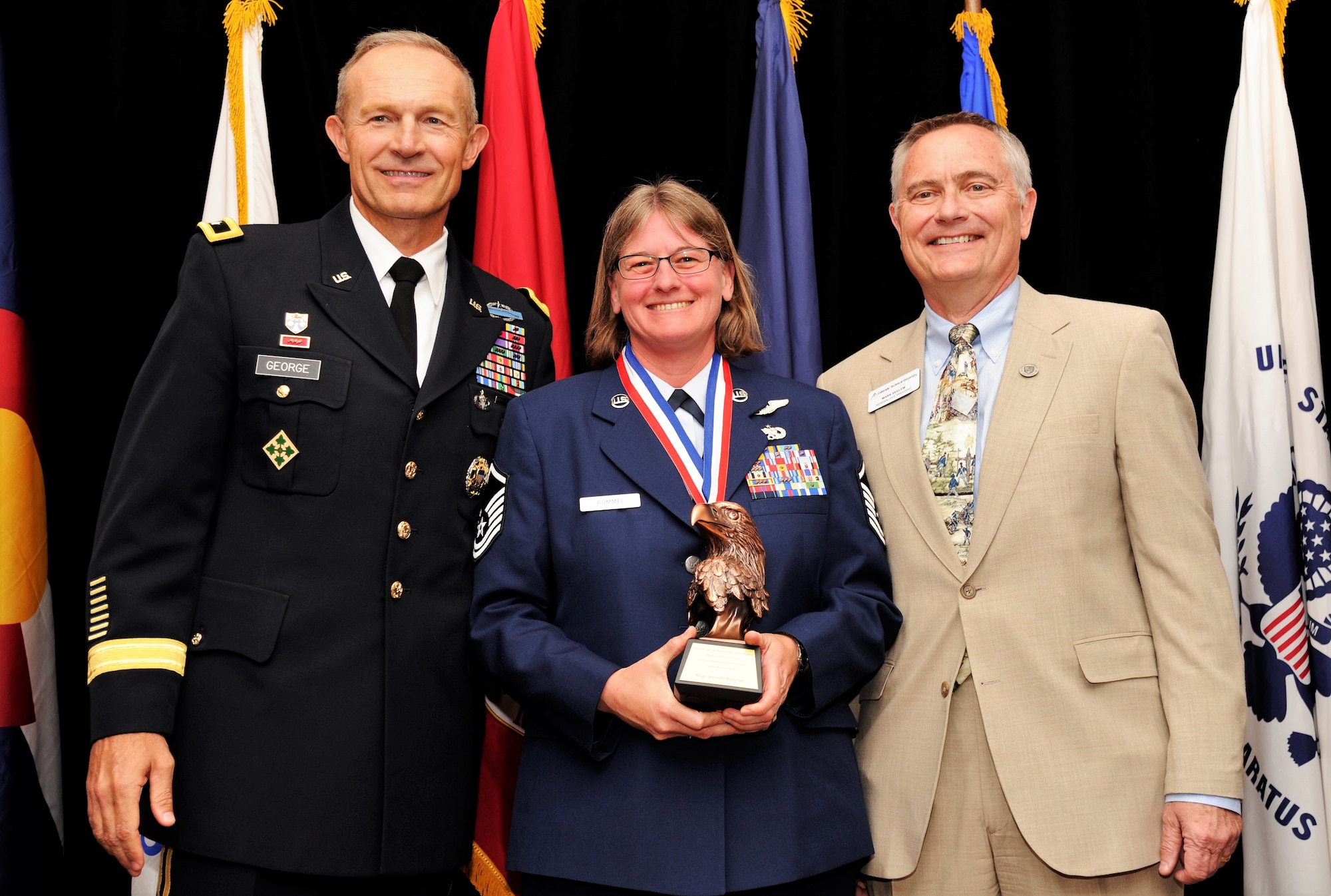 Master Sgt. Jeanette Rummel, a 731st Airlift Squadron evaluator flight engineer, poses for a photo with U.S. Army Maj. Gen. Randy George, the 4th Infantry Division commander, left, and Mark Seglem, the regional vice president of Colorado Campuses, right, during the 2018 Armed Forces Luncheon, in Colorado Springs, Colorado, May 17, 2018.