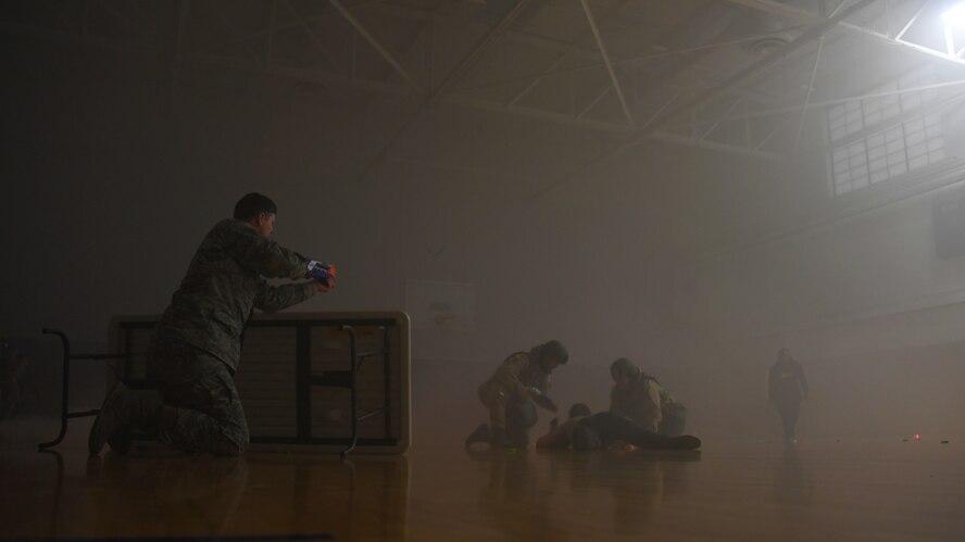 Staff Sgt. Jacob Williams, unit deployment manager with the 319th Logistics Readiness Squadron, left, simulates a combat environment by firing foam darts towards team members of the 319 LRS as they provide self-aid and buddy care during a readiness competition May 18, 2018, on Grand Forks Air Force Base, North Dakota. The readiness competition consisted of 10 stations meant to test Airmen on their knowledge and application of SABC, chemical, biological, radiological and nuclear weapon safety, map-reading, hand-to-hand combat, weapons assembly and more. (U.S. Air Force photo by Airman 1st Class Elora J. Martinez)