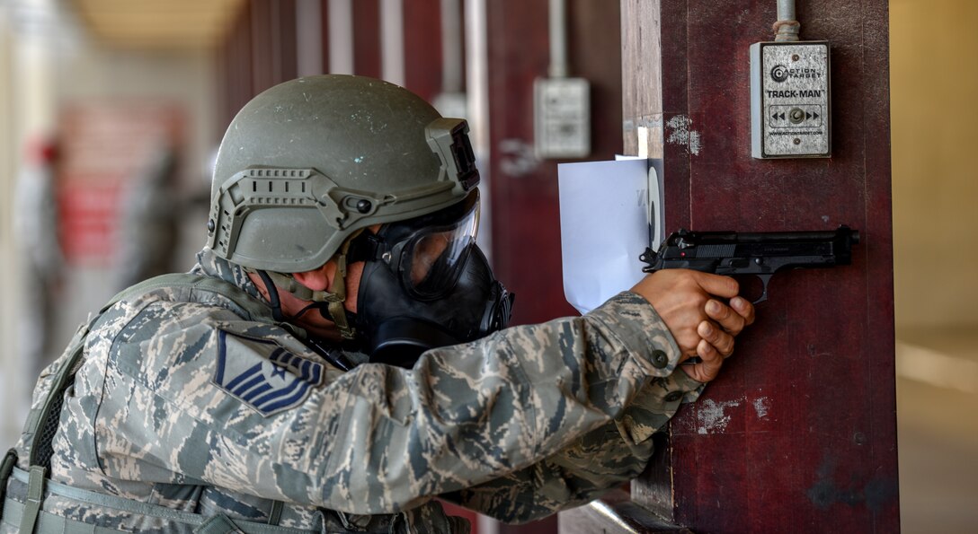 Airmen braces himself against wooden beam while firing in M9 pistol firing competition.