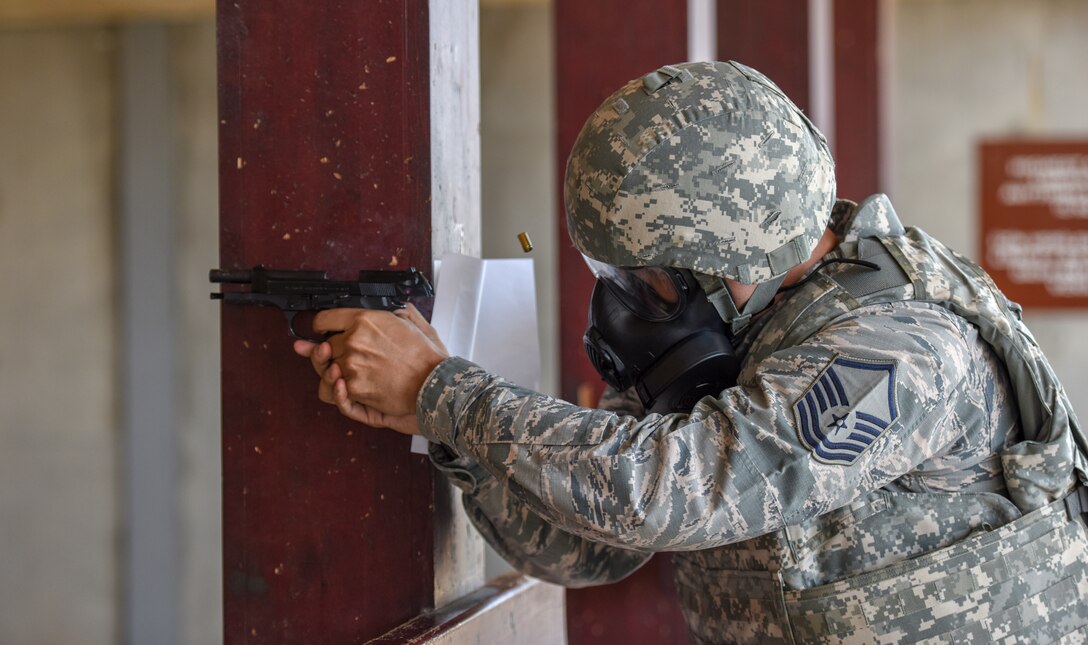 Airmen fires M9 during pistol firing competition while wearing gas mask.