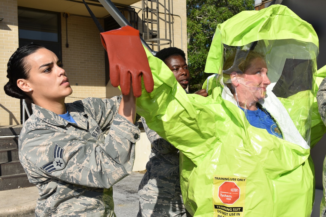 An airman helps another airman put on a protective suit.