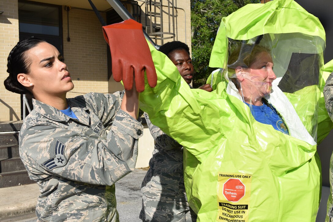 An airman helps another airman put on a protective suit.