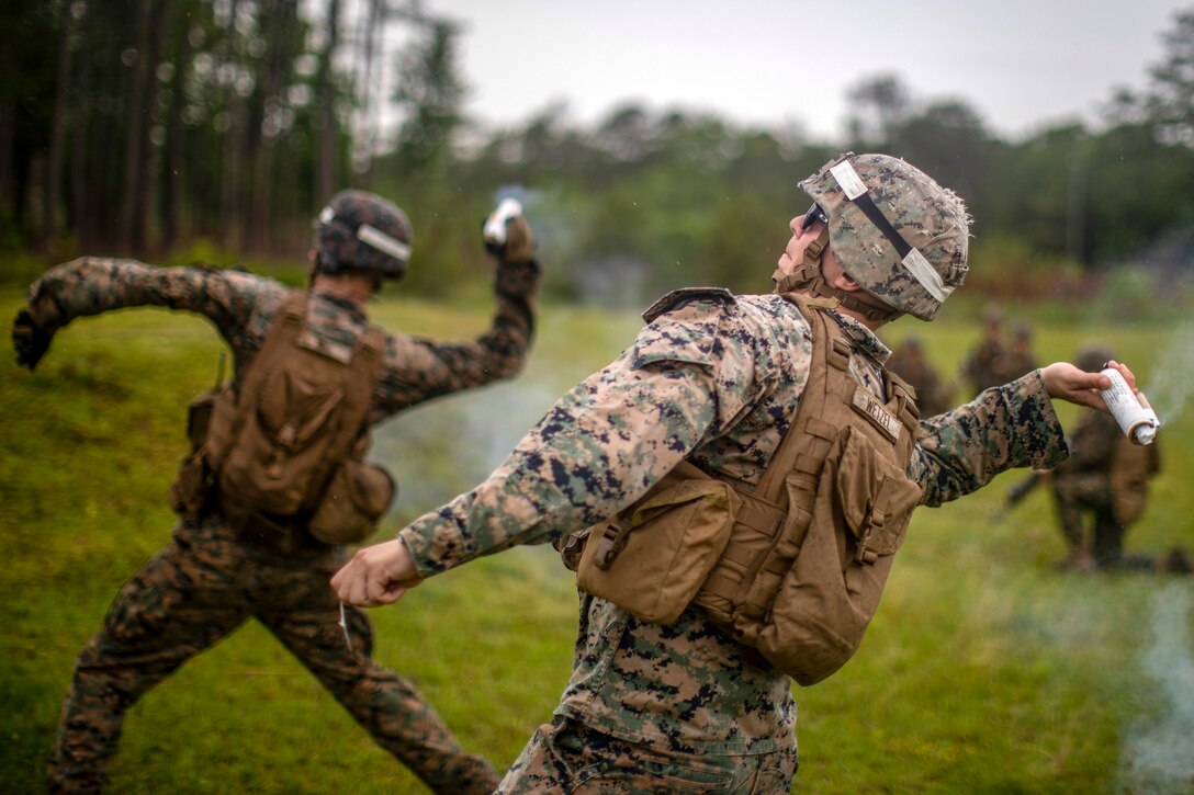 A Marine leans back with a projectile in his hand before tossing it, as another Marine does the same in the background.