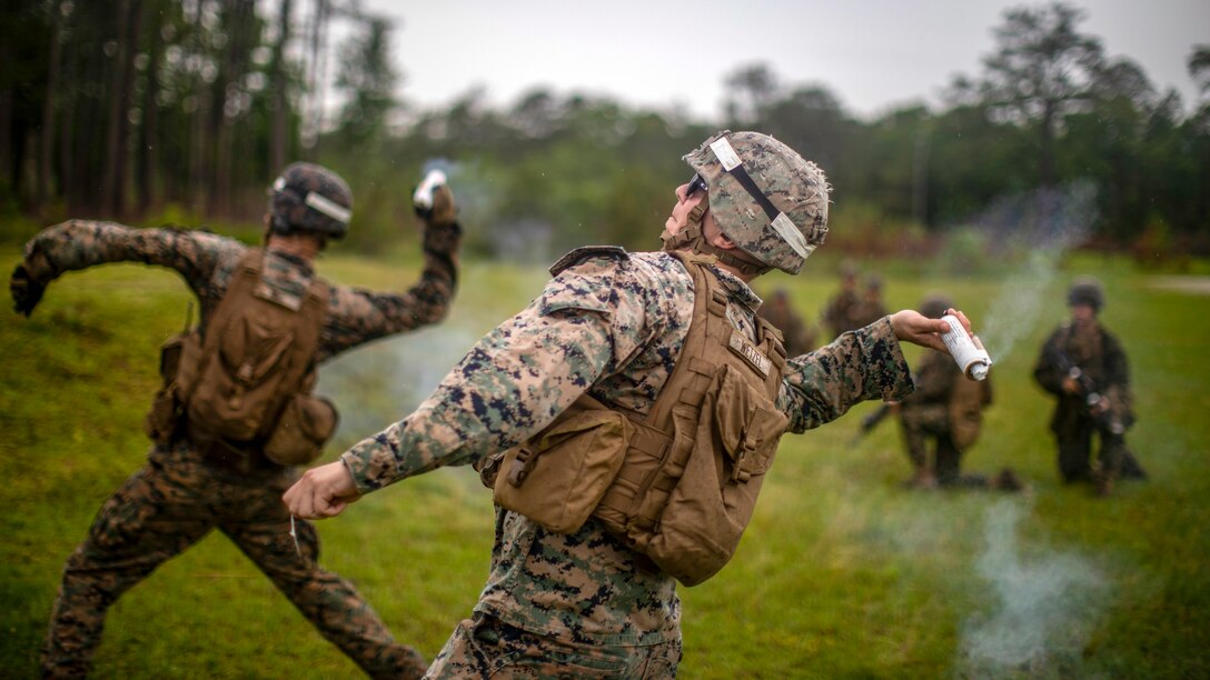 A Marine leans back with a projectile in his hand before tossing it, as another Marine does the same in the background.