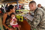 An airman speaks to a woman holding a child on her lap.