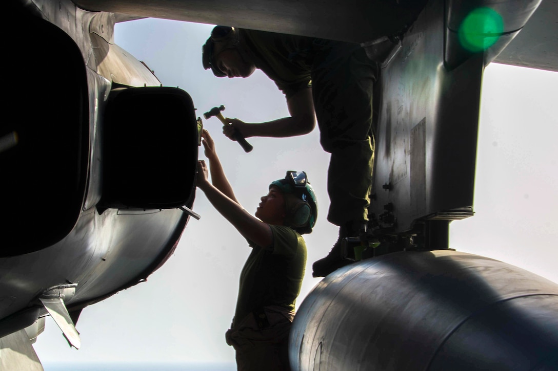 Two Marines, shown in silhouette, perform maintenance on an aircraft.