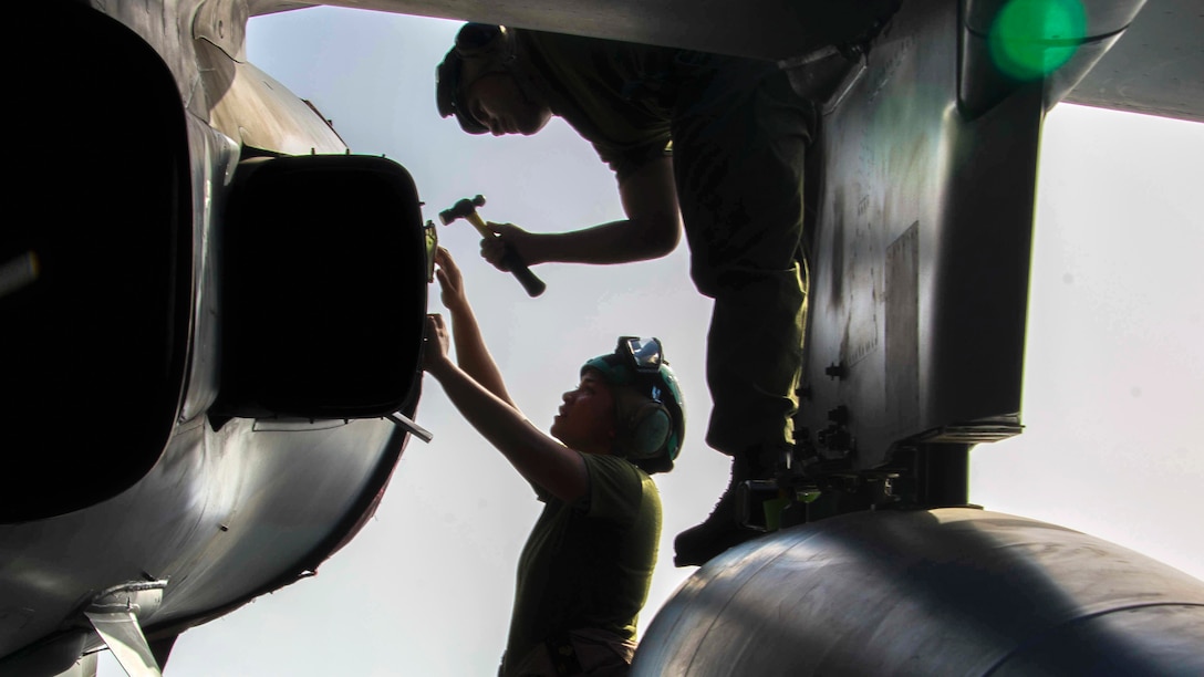Two Marines, shown in silhouette, perform maintenance on an aircraft.