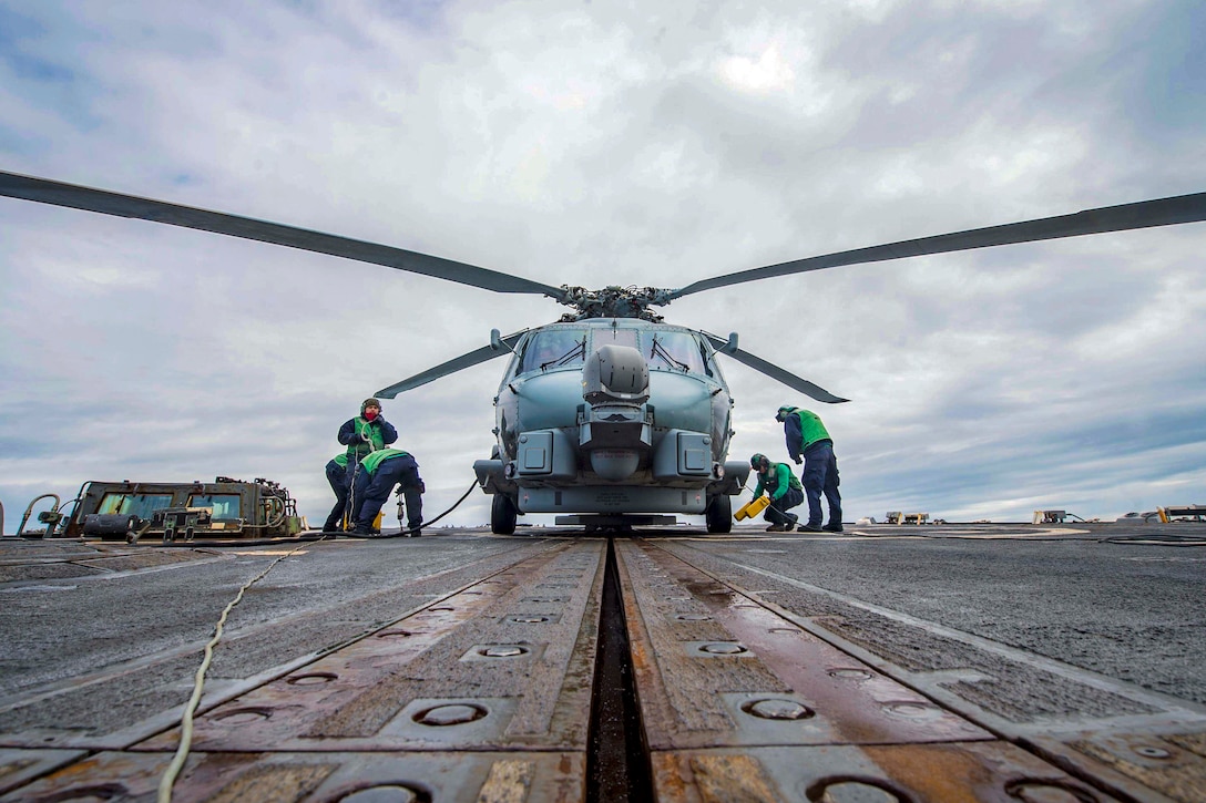 Sailors work on a helicopter on a ship's flight deck.