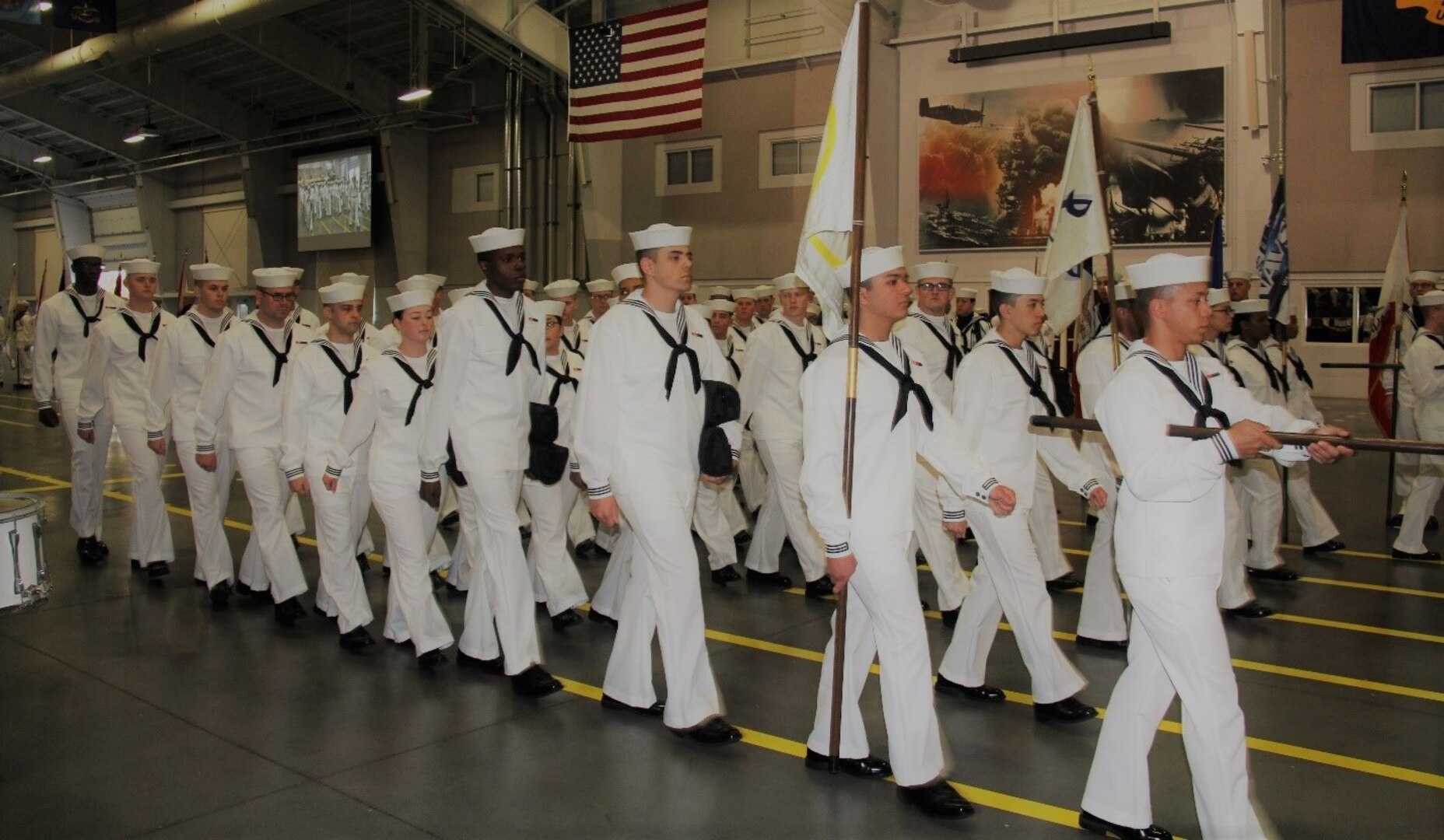 IMAGE: GREAT LAKES, Ill. (May 18, 2018) - Recruit Division 213 marches with the Naval Surface Warfare Center Dahlgren Division Dam Neck Activity flag (blue, at right) at their graduation ceremony. NSWCDD Dam Neck Activity Commanding Officer Cmdr. Andrew J. Hoffman led a contingent at graduation after another contingent participated in the division's Battle Stations 21 drills and Capping Ceremony earlier in the week.