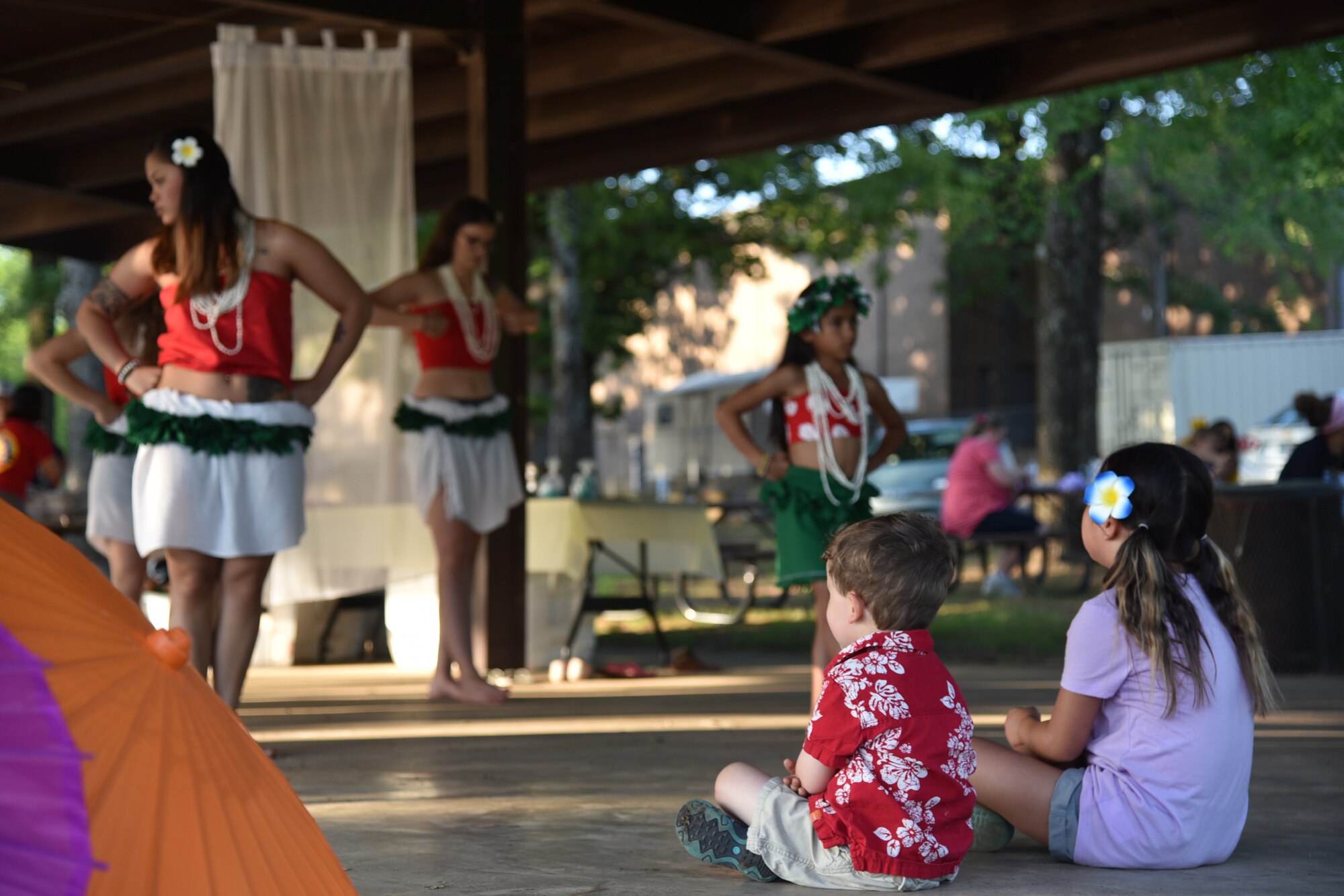 People dance outdoors in colorful clothing in front of an audience.