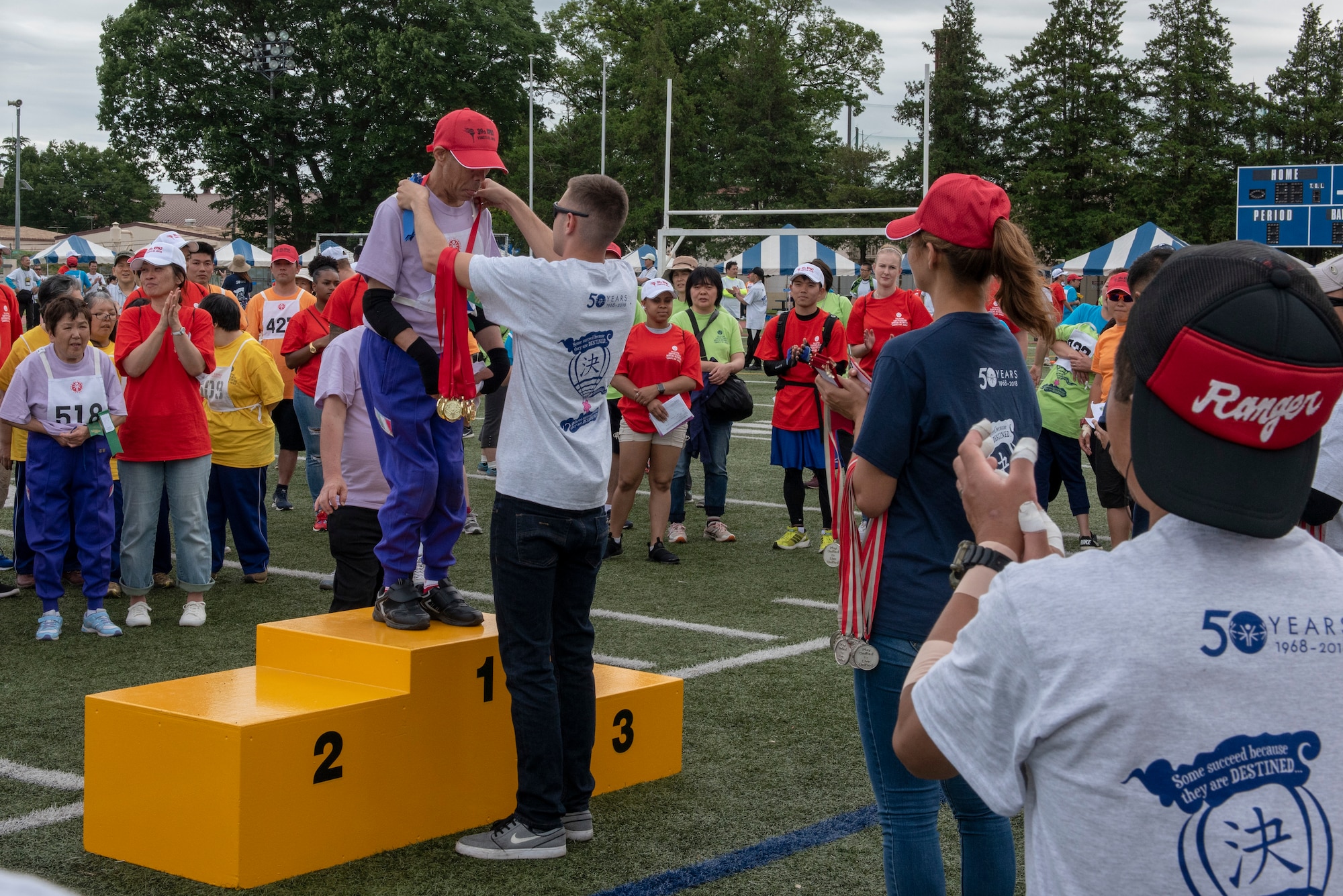An athlete receives a gold medal as participants cheer him on for his success during the Kanto Plains Special Olympics at Yokota Air Base, Japan, May 19, 2018.