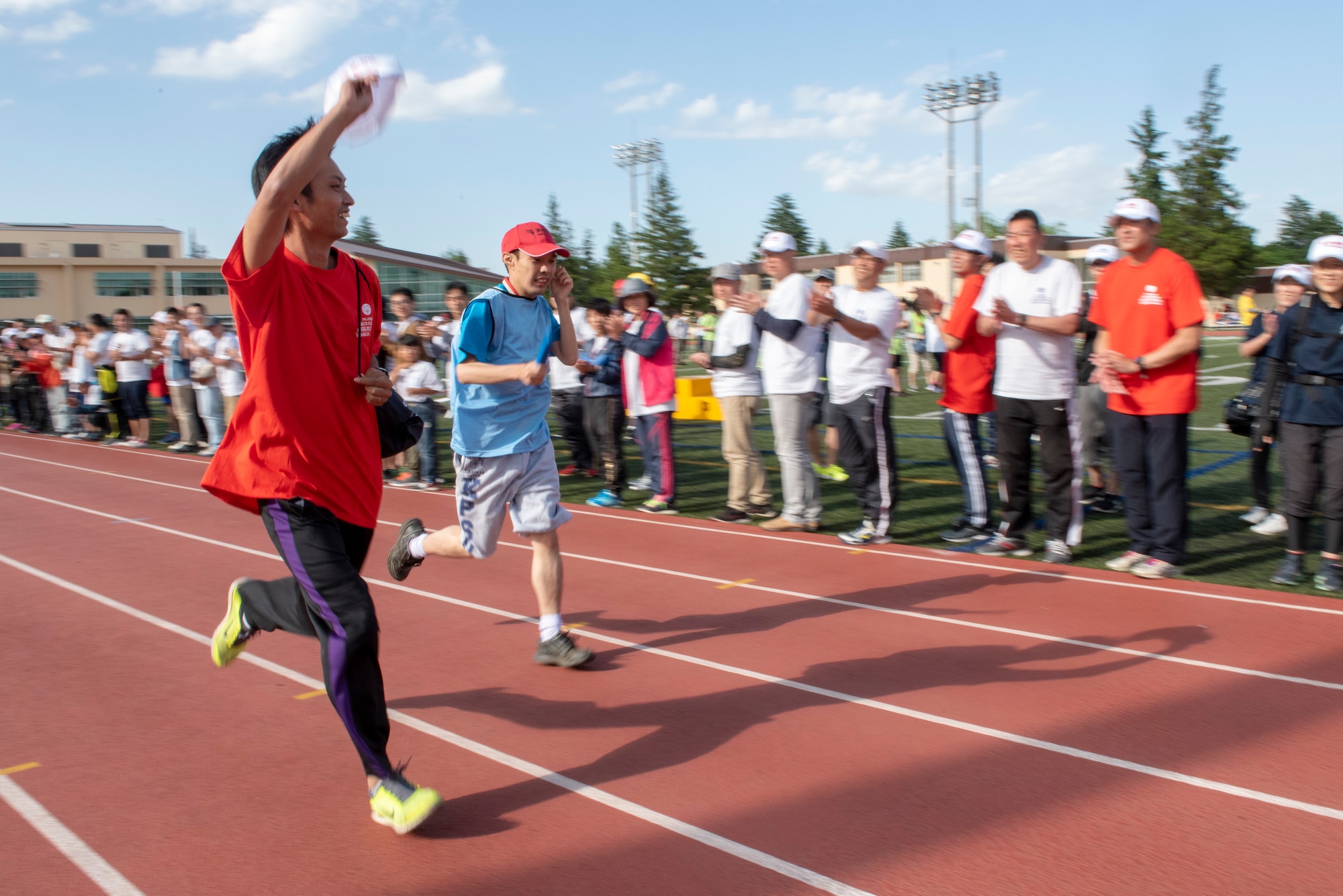 An athlete buddy sprints next to his athlete as the crowd cheers them on during the 4x100 meter relay race during the Kanto Plains Special Olympics at Yokota Air Base, Japan, May 19, 2018.