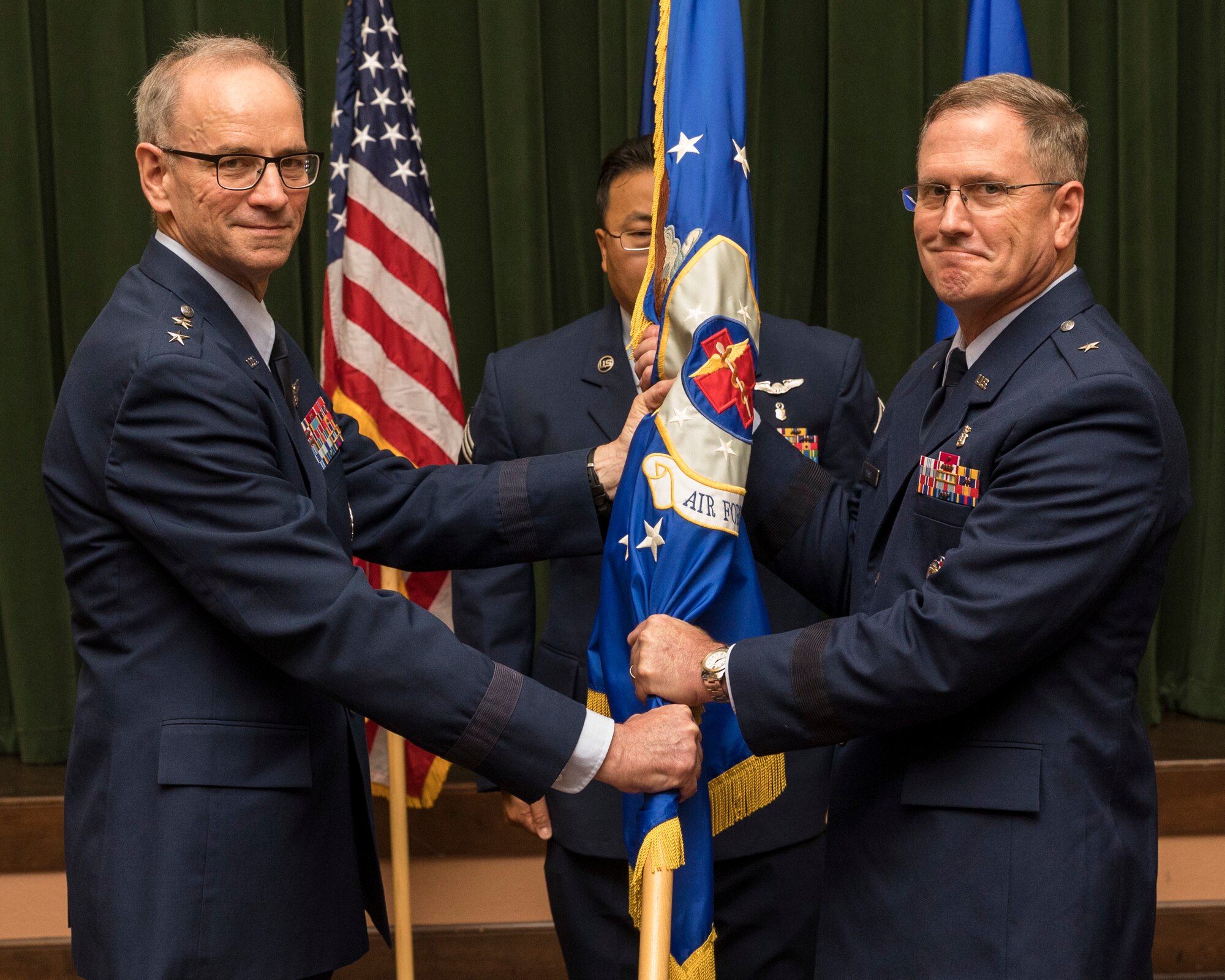 Lt. Gen. Mark A. Ediger, U.S. Air Force Surgeon General, facilitates the passing of the guidon to Brig. Gen. James H. Dienst, Air Force Medical Operations Agency commander, during a change of command ceremony at Joint Base San Antonio-Lackland, Texas, May 22, 2018. (U.S Air Force photo by Ismael Ortega)
