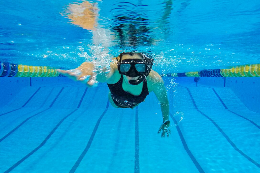A sailor wearing a mask and snorkel swims forward in a pool lane.