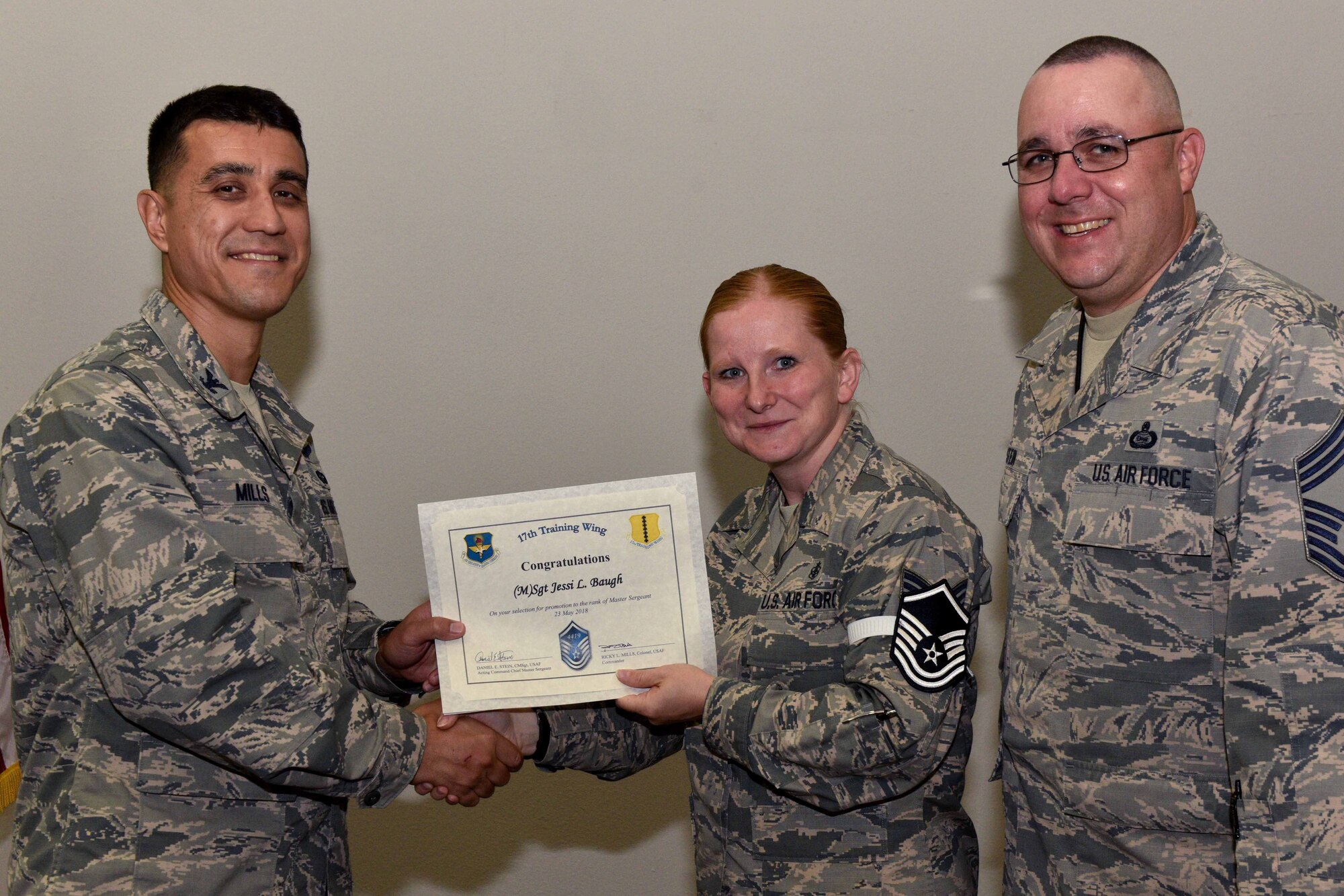 U.S. Air Force Col. Ricky Mills, 17th Training Wing commander, presents Tech. Sgt. Jessi Baugh, 17th Medical Support Squadron technician, their certificate of selection with Chief Master Sgt. Daniel Stein, 17th TRW command chief, during a Master Sergeant release party at the Event Center on Goodfellow Air Force Base, Texas, May 25, 2018. Goodfellow held the party to notify the selected promotees and to give fellow wingmen and friends an opportunity to congratulate them on their success. (U.S. Air Force photo by Senior Airman Randall Moose)