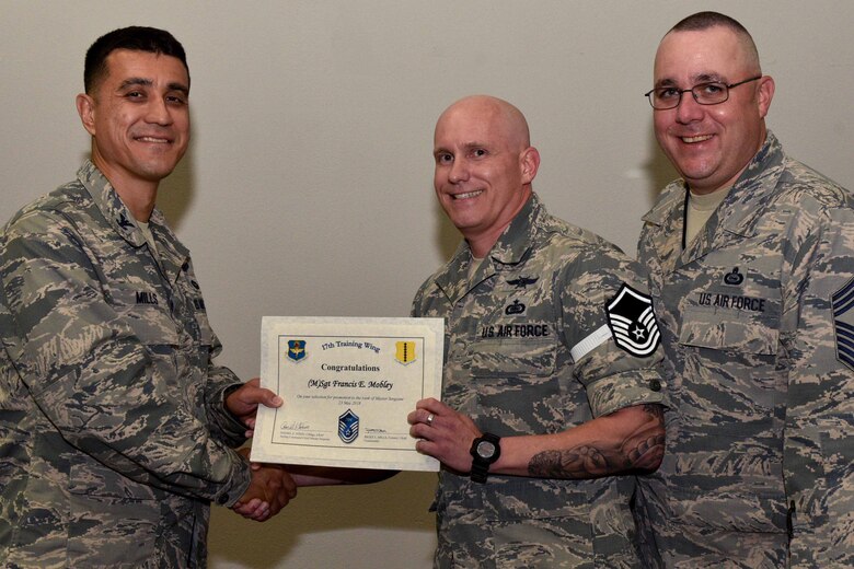 U.S. Air Force Col. Ricky Mills, 17th Training Wing commander, presents Tech. Sgt. Francis Mobley, 316th Training Squadron instructor, their certificate of selection with Chief Master Sgt. Daniel Stein, 17th TRW command chief, during a Master Sergeant release party at the Event Center on Goodfellow Air Force Base, Texas, May 25, 2018. Goodfellow held the party to notify the selected promotees and to give fellow wingmen and friends an opportunity to congratulate them on their success. (U.S. Air Force photo by Senior Airman Randall Moose)