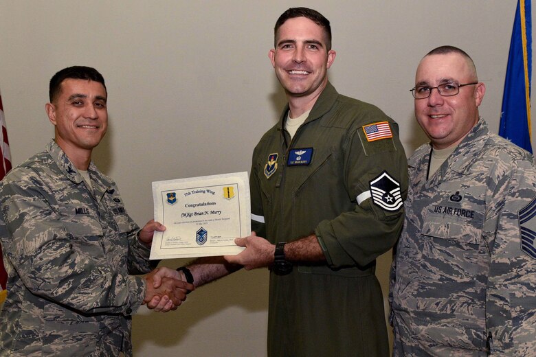 U.S. Air Force Col. Ricky Mills, 17th Training Wing commander, presents Tech. Sgt. Brian Murry, 316th Training Squadron instructor, their certificate of selection with Chief Master Sgt. Daniel Stein, 17th TRW command chief, during a Master Sergeant release party at the Event Center on Goodfellow Air Force Base, Texas, May 25, 2018. Goodfellow held the party to notify the selected promotees and to give fellow wingmen and friends an opportunity to congratulate them on their success. (U.S. Air Force photo by Senior Airman Randall Moose)