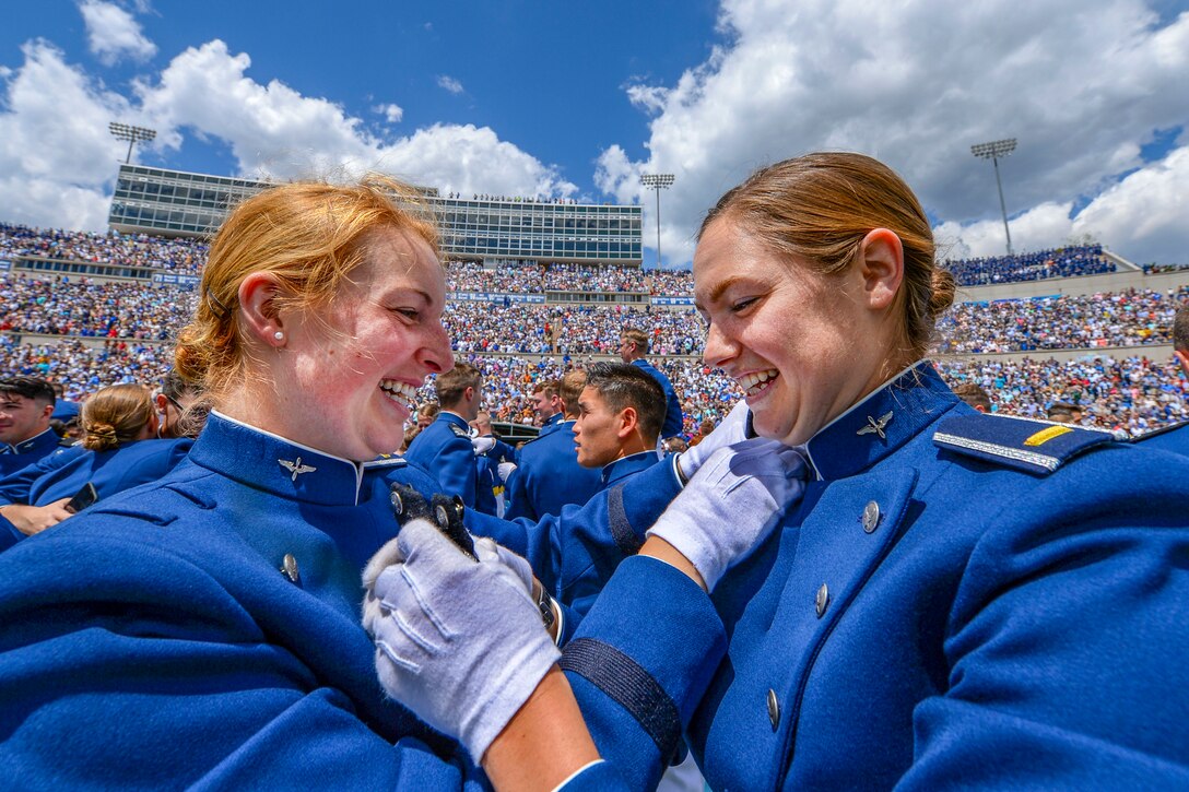 Two smiling airmen pin rank insignia on each other in a packed stadium.