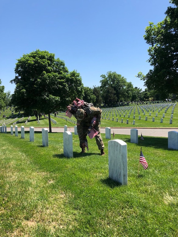 Soldier places a flag on a grave in Arlington National Cemetery.