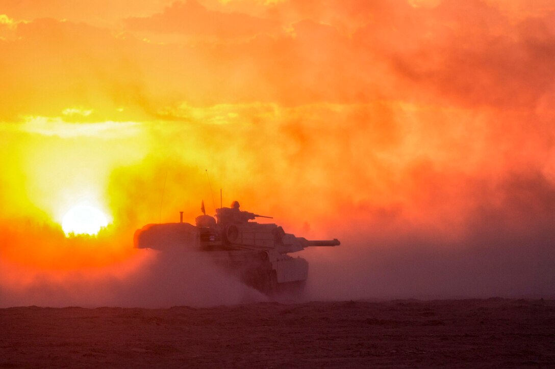 A tank kicks up sand while driving on a field, illuminated by orange sky.