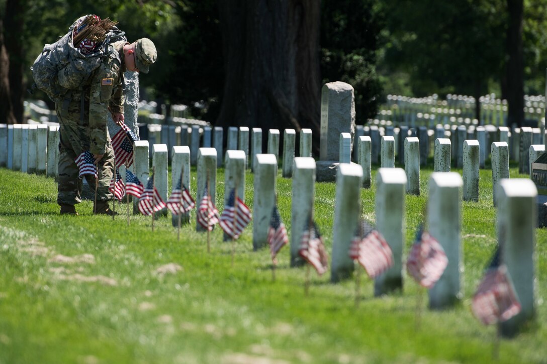 A soldier places American flags in front of headstones at Arlington National Cemetery.