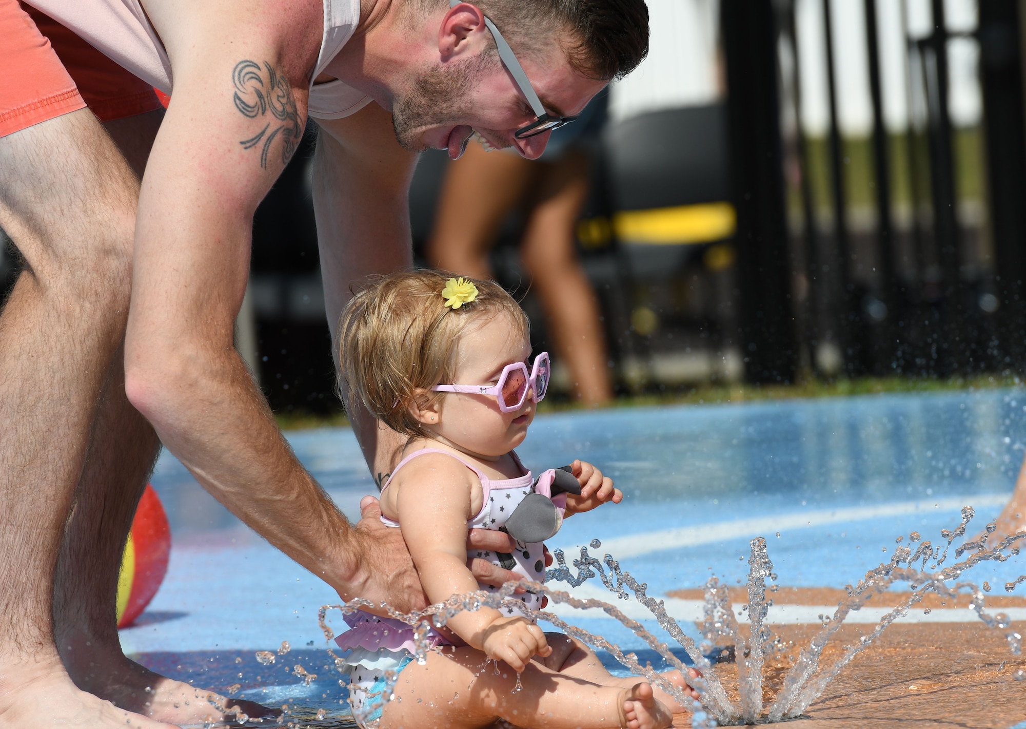 U.S. Navy Constructionman Tyler Randall, Naval Mobile Construction Battalion One, at the Naval Construction Battalion Center, in Gulfport, Mississippi, plays with his daughter, Emma, on the splash pad during the Splash Pad Ribbon Cutting Ceremony at the West Falcon Housing area in Biloxi, Mississippi, May 22, 2018. The Hunt Company project will provide more recreational activities for all Keesler family housing families. (U.S. Air Force photo by Kemberly Groue)