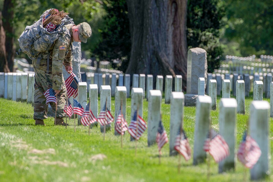 A soldier places American flags in front of headstones at Arlington National Cemetery
