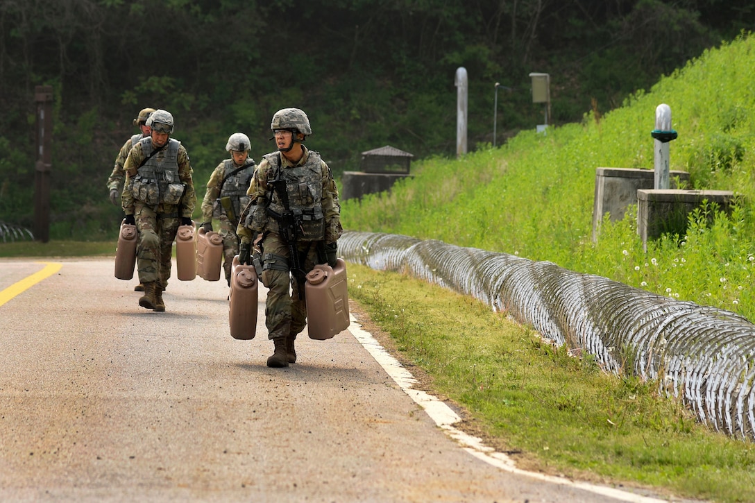 Soldiers carry 5-gallon water containers at the stress shoot event.