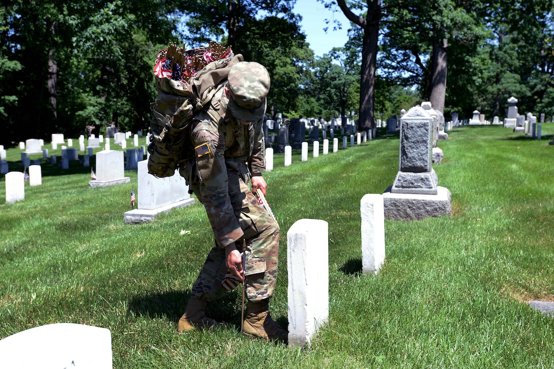 A soldier places an American flag in front of a headstone.