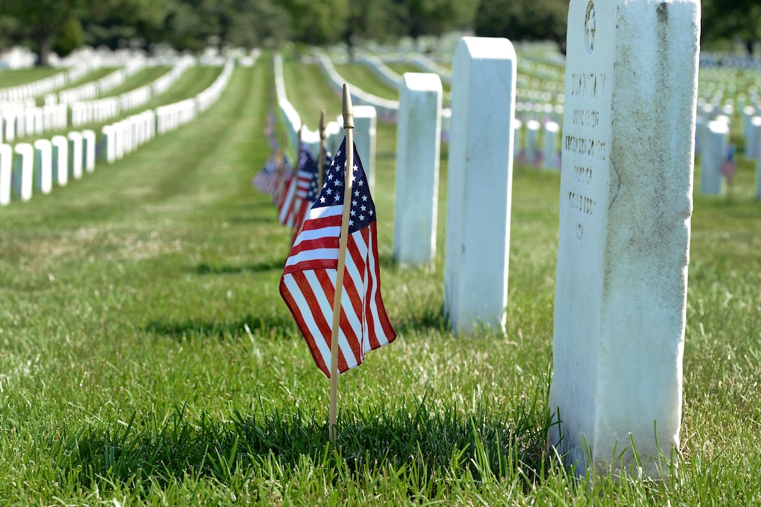 American flags stand in front of headstones at Arlington National Cemetery.
