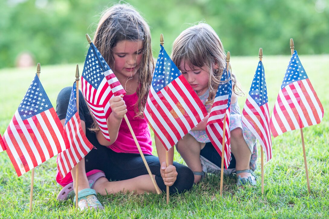 Two young girls place American flags in the ground.