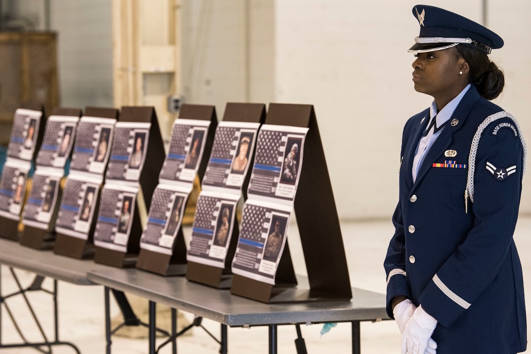 An airman stands beside 14 placards in a room.