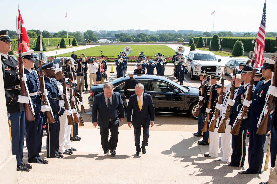 Defense Secretary James N. Mattis walks up the steps with another person.