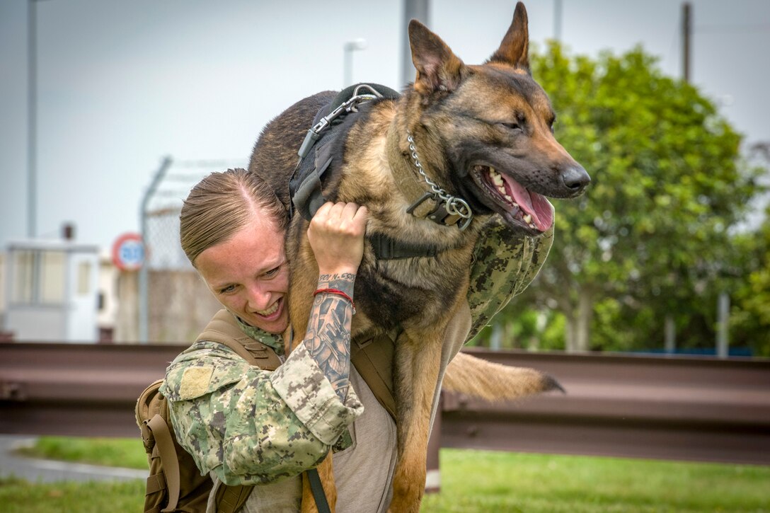 A sailor carriers a German shepherd-type dog on one shoulder.