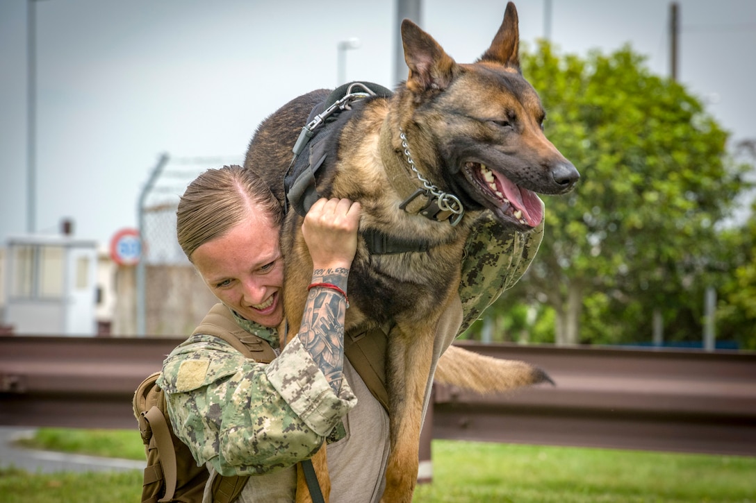 A sailor carriers a German shepherd-type dog on one shoulder.