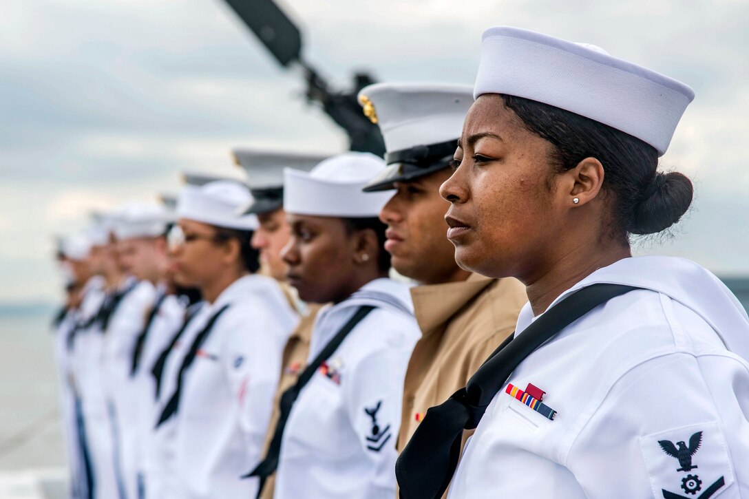 Sailors and Marines stand in a row aboard a ship.