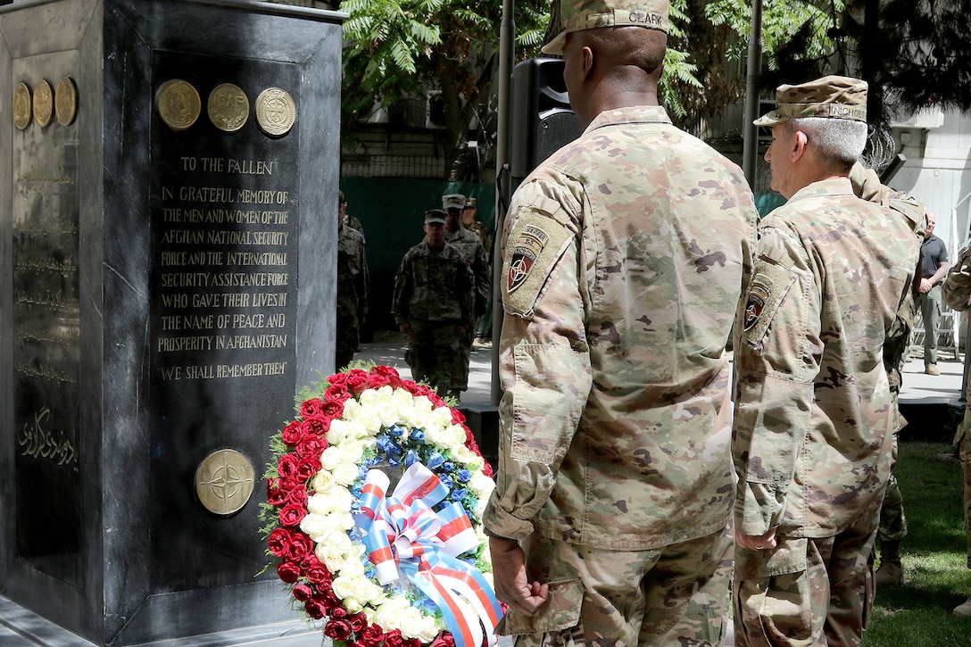 Two soldiers salute a wreath and monument.