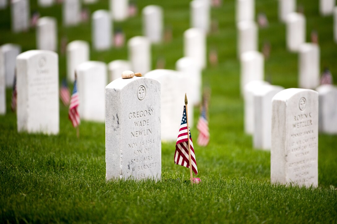 Rows of headstones with American flags sit in the grass.